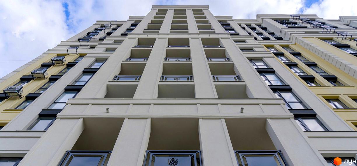 Висока будівля ЖК Prestige Apartments з балконами та вікнами. Фасад будинку виконано у світлих тонах, видно блакитне небо з хмарами.
