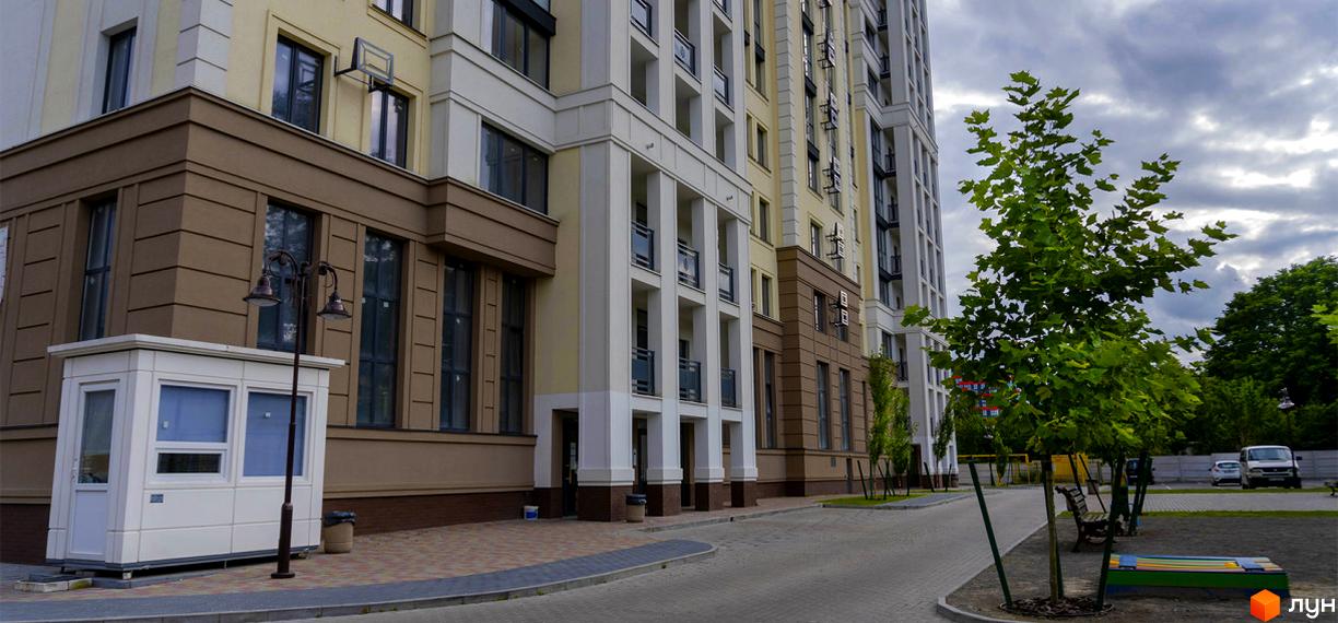 Зовнішній вигляд будинку ЖК Prestige Apartments. На території є дерева, лавки та дитячий майданчик.