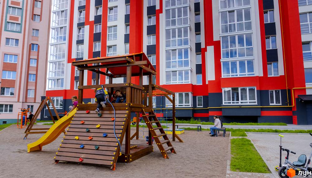 Житловий комплекс Корольова: яскрава фасадна частина будівель з червоними та білими смугами, дитячий майданчик з гіркою та скеледромом.