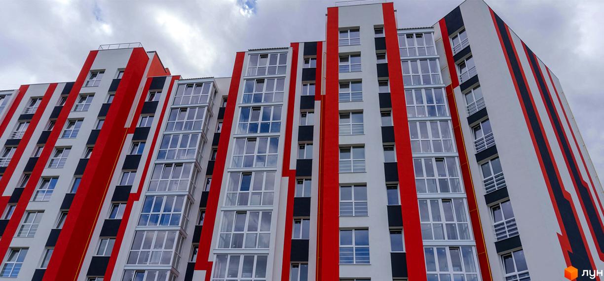 Зовнішній вигляд житлового комплексу Корольова з фасадом у червоно-чорно-білих тонах та великою кількістю скління. Будинок має геометричні форми та виступаючі елементи.