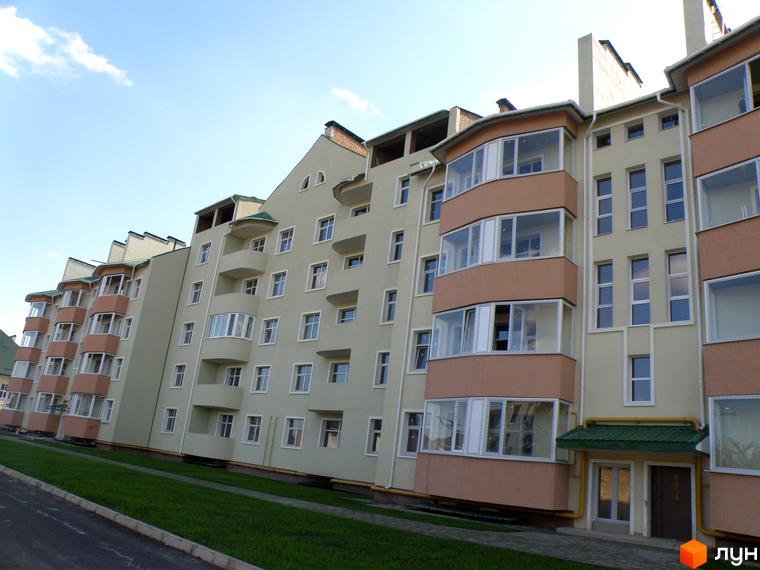 Фасад Житлового комплексу Петропавлівський світлого кольору з заскленими балконами та зеленим дахом. Перед будинком розташований зелений газон та пішохідна доріжка.