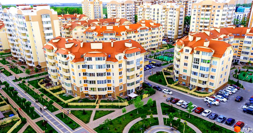 Житловий комплекс Петрівський квартал з жовто-бежевими фасадами та червоними дахами. На прибудинковій території зелені газони, доріжки та дитячі майданчики.