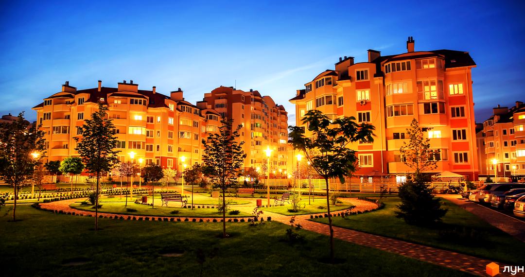 Житловий комплекс Петрівський квартал з підсвіченими вікнами та доглянутою прибудинковою територією з доріжками та зеленими насадженнями.