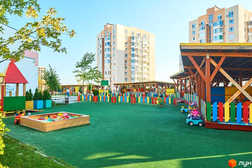 Житловий комплекс Петрівський квартал: багатоповерхові будинки та дитячий майданчик з різнокольоровою огорожею. Територія комплексу з пісочницею та ігровими елементами.