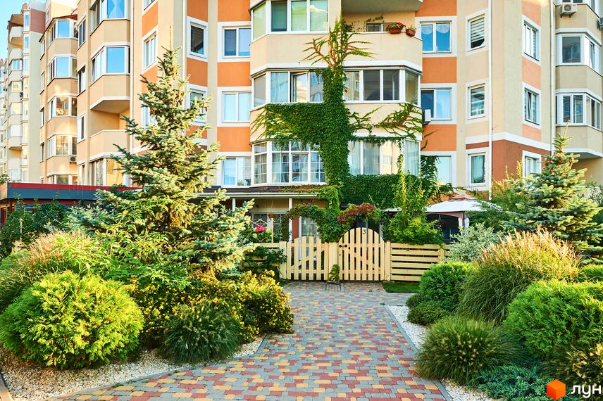 Житловий комплекс Петрівський квартал з доглянутою прибудинковою територією та зеленими насадженнями. Фасад будинку оздоблений в помаранчево-бежевих тонах.
