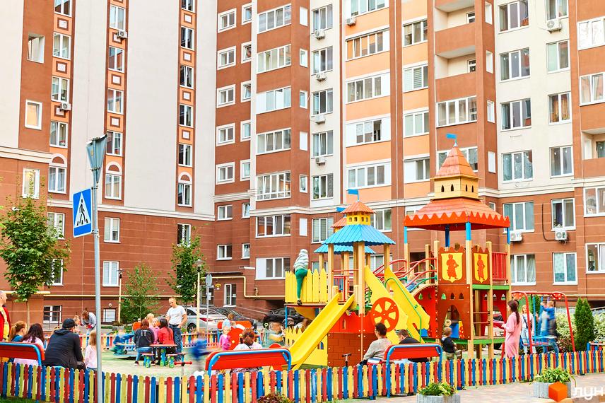 Житловий комплекс Петрівський квартал з яскравим дитячим майданчиком та зонами відпочинку. Багатоповерхові будинки з коричневими та білими фасадами.