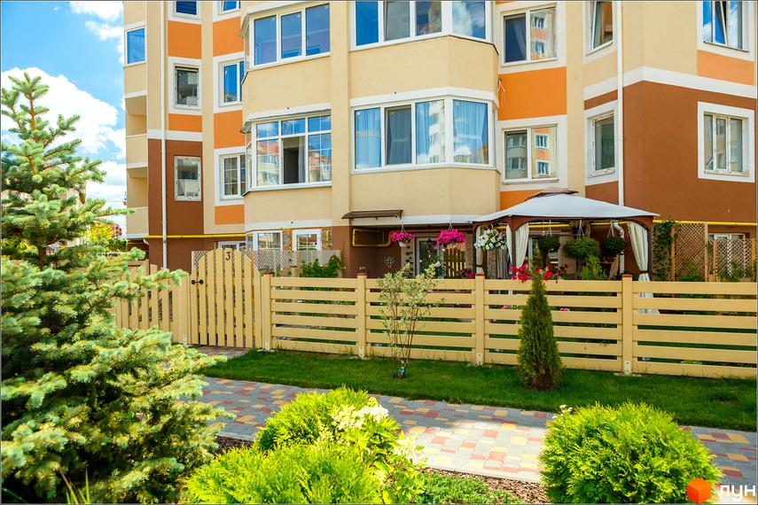 Житловий комплекс Петрівський квартал з фасадом в бежево-помаранчевих тонах та огородженою прибудинковою територією з зеленими насадженнями.