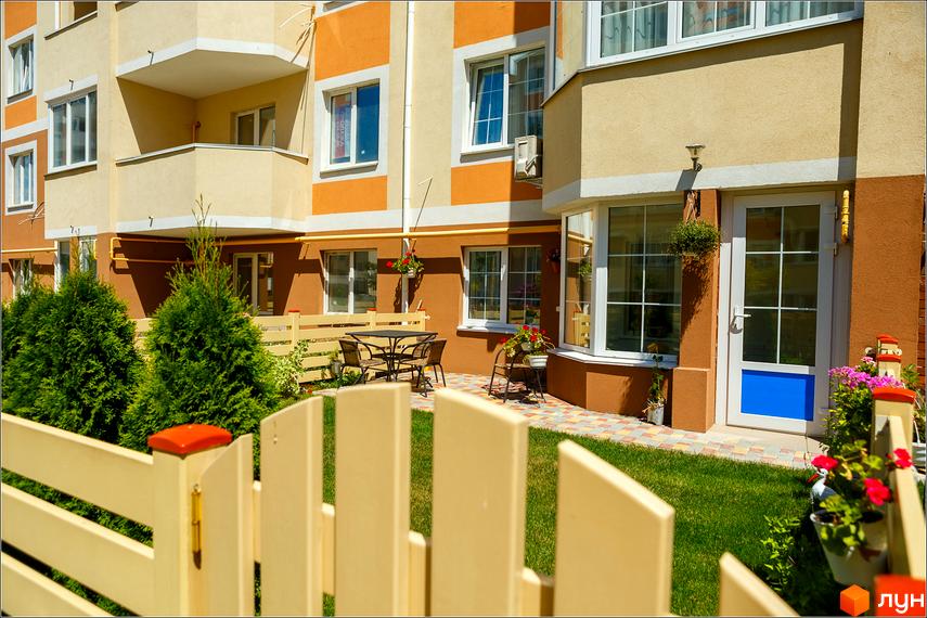 Житловий комплекс Петрівський квартал. Фасад будинку з балконами, вікнами та дверима. Прибудинкова територія з газоном, деревами та зоною відпочинку.