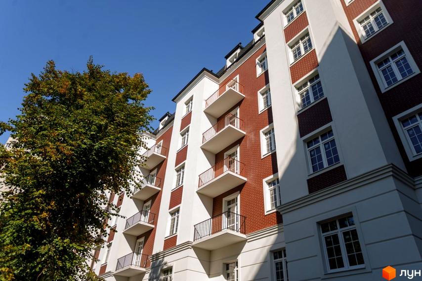 Житловий комплекс Notting Hill: будівля з білим фасадом, червоною цеглою, білими вікнами та балконами. Поруч велике зелене дерево.