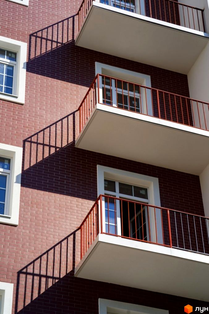 Зовнішній вигляд фасаду житлового комплексу Notting Hill з цегляним оздобленням та балконами з червоними перилами. На стіні будинку видно тіні від перил.