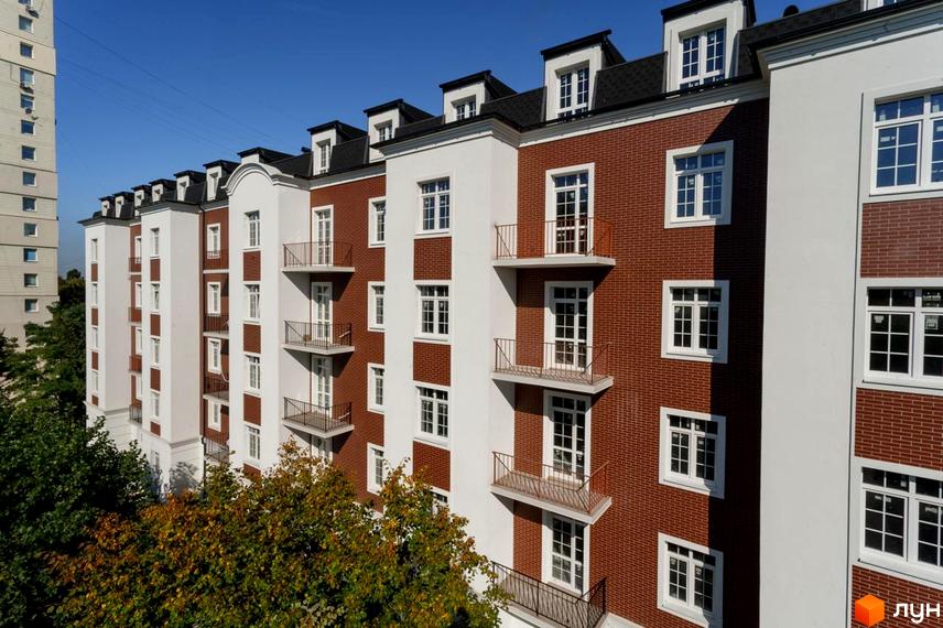 Фасад житлового комплексу Notting Hill з червоної цегли та білої штукатурки, з балконами та мансардними вікнами. Навколо зелені дерева.