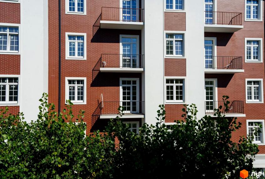 Фасад новобудови ЖК Notting Hill з червоної цегли та білими елементами, вікнами та балконами. Зелені дерева перед будинком.