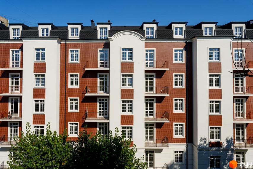 Фасад житлового комплексу Notting Hill з цегляним оздобленням та білими елементами, вікнами та балконами на тлі блакитного неба.
