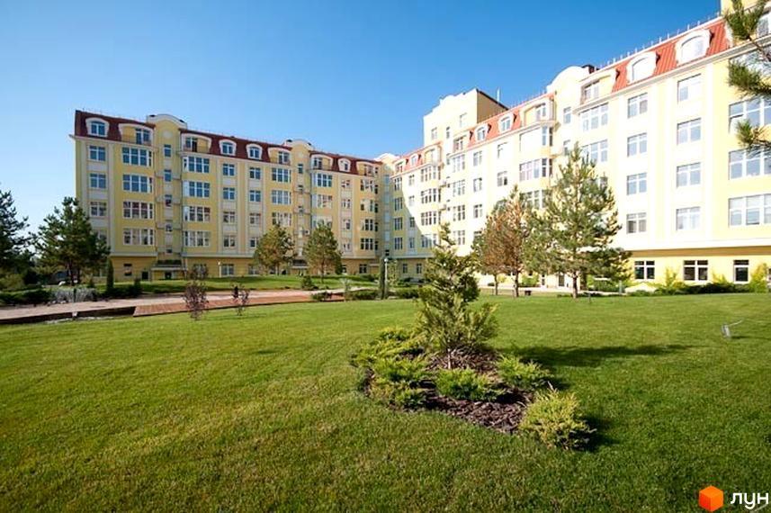 Житловий комплекс Щасливе з жовтою фасадною частиною та зеленою прибудинковою територією, облаштованою газоном і деревами.