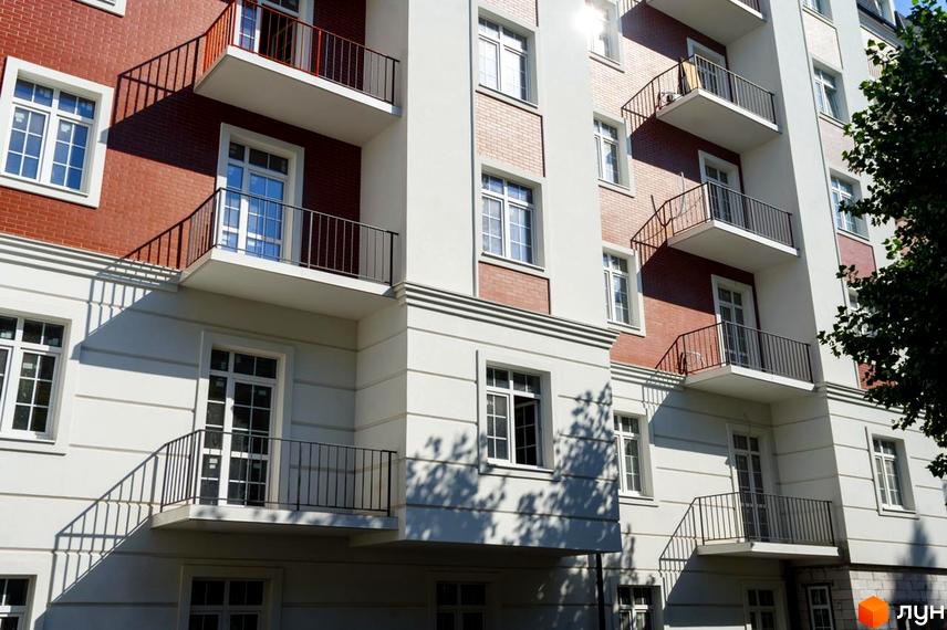 Фасад Житлового комплексу Notting Hill з білими елементами та червоною цеглою, балкони з металевими поручнями. Видно тіні та зелене дерево.