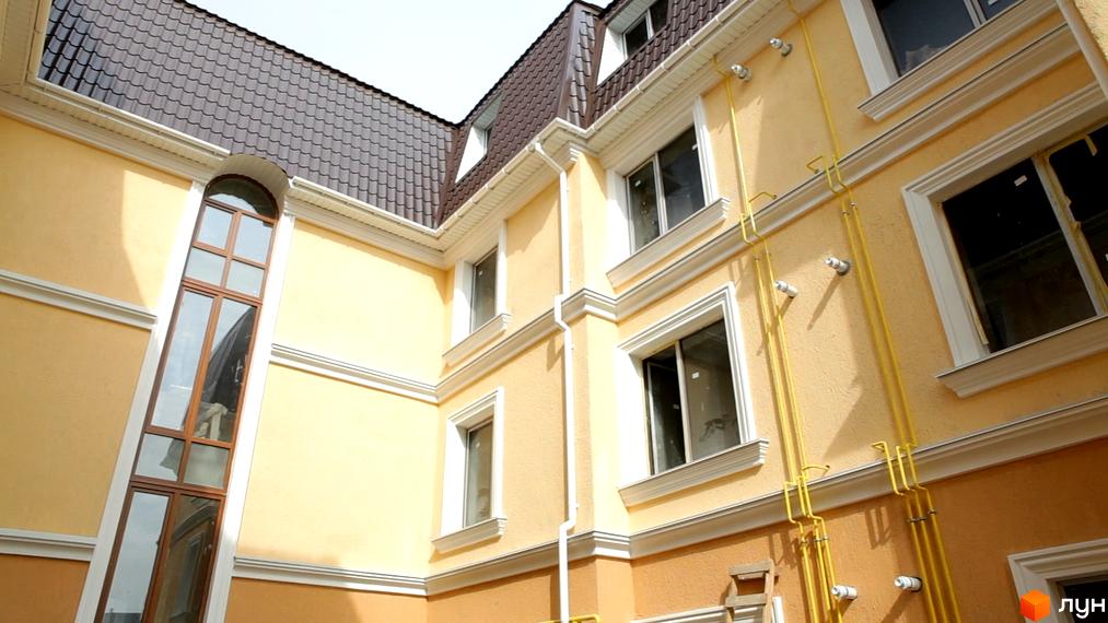 Зовнішній вигляд будинку житлового комплексу Леваневський: фасад з вікнами, дах з черепицею, жовтий колір стін. Архітектура будівлі, елементи декору.