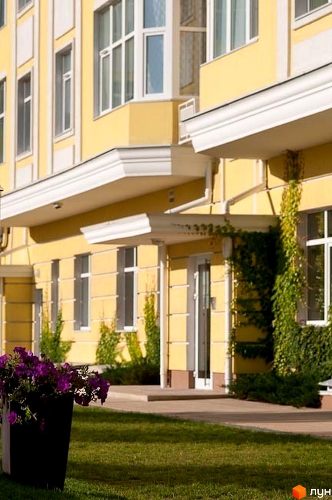 Житловий комплекс Щасливе з жовтими фасадами та великими вікнами. Прибудинкова територія озеленена квітами та газоном.