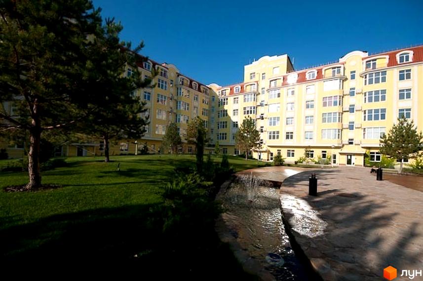 Житловий комплекс Щасливе з жовтою фасадною частиною та прибудинковою територією з зеленими насадженнями і фонтаном.