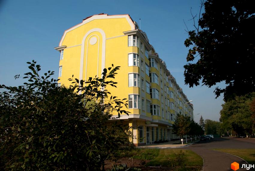 Житловий комплекс Щасливе з яскраво-жовтою фасадною стіною та великими вікнами. Прибудинкова територія озеленена деревами та кущами.