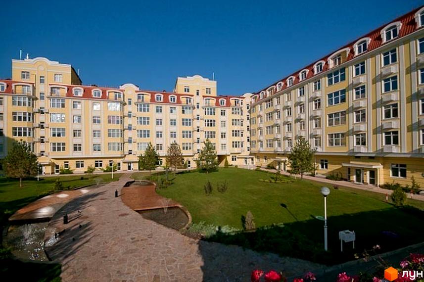 Житловий комплекс Щасливе з жовтою фасадною обробкою та червоним дахом, зелена прибудинкова територія з доріжками.