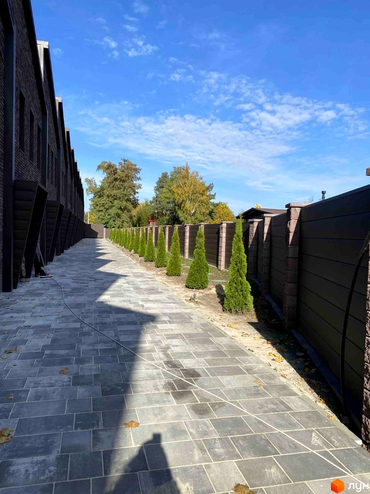 Таунхаус Forest Park Hora з брукованою доріжкою та акуратними туями вздовж паркану. Зовнішній вигляд новобудови та прибудинкової території.