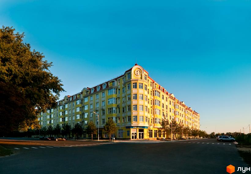 Житловий комплекс Щасливе з жовтою фасадною частиною та зеленими насадженнями на прибудинковій території.