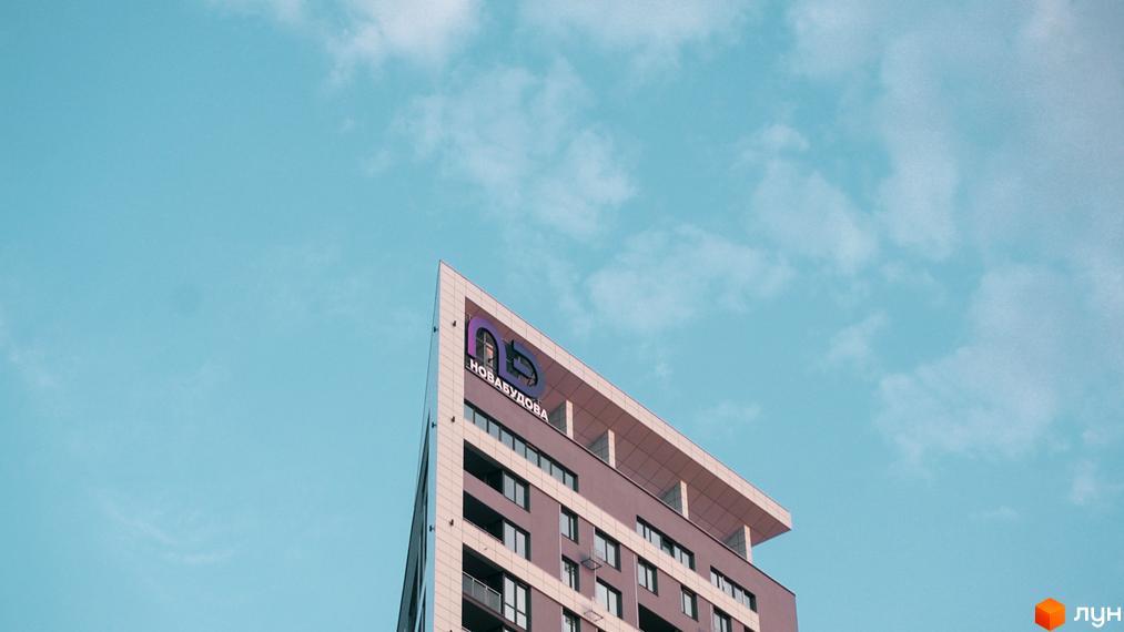 Фасад житлового комплексу Щасливий Platinum з логотипом компанії на верхньому поверсі на фоні блакитного неба з хмарами.