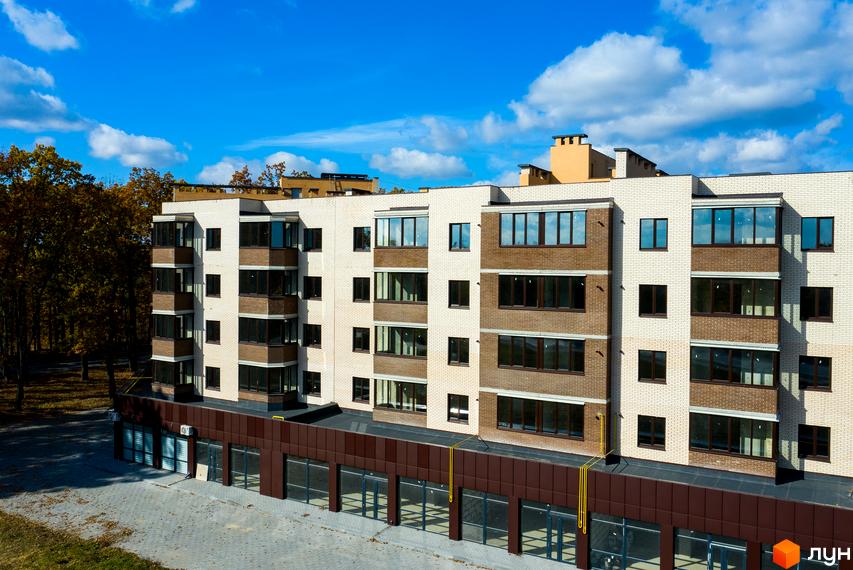 Новобудова ЖК Софія з цегляним фасадом світлого та коричневого кольору, великими вікнами та балконами. Поруч розташований парк з осінніми деревами та вимощена бруківкою територія.