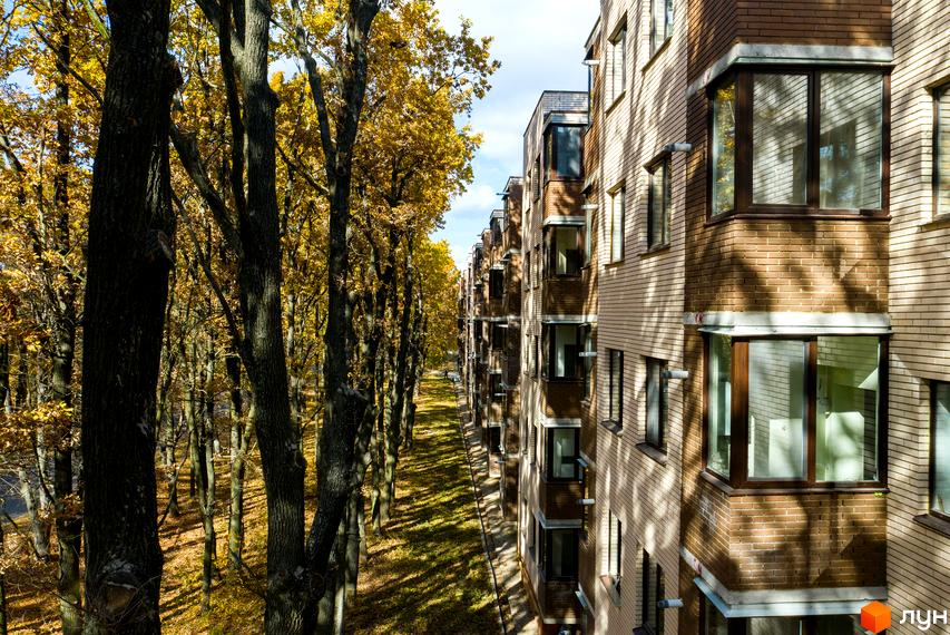 Житловий комплекс Софія: багатоповерховий будинок зі світлої цегли та темними вікнами. Поруч розташований осінній парк з деревами та опалим листям.