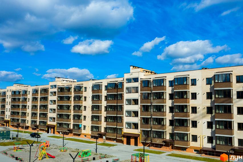 Новобудова ЖК Софія. Фасад будинку оздоблений світлою цеглою, з великими вікнами та балконами. Поруч дитячий майданчик з гойдалками та гірками.