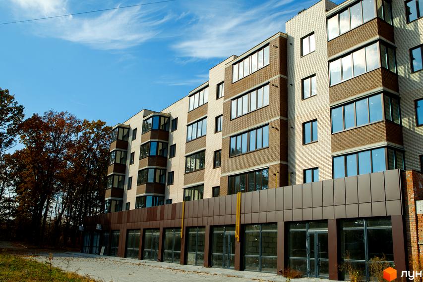 Фасад житлового комплексу Софія з цегляним оздобленням та великими вікнами. Навколо будівлі розташована прибудинкова територія з деревами та тротуаром.