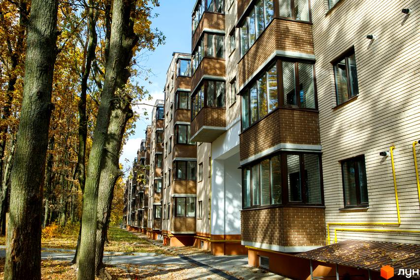 Зовнішній вигляд житлового комплексу Софія з цегляним фасадом та балконами. Навколо комплексу дерева з осіннім листям та зеленою травою.