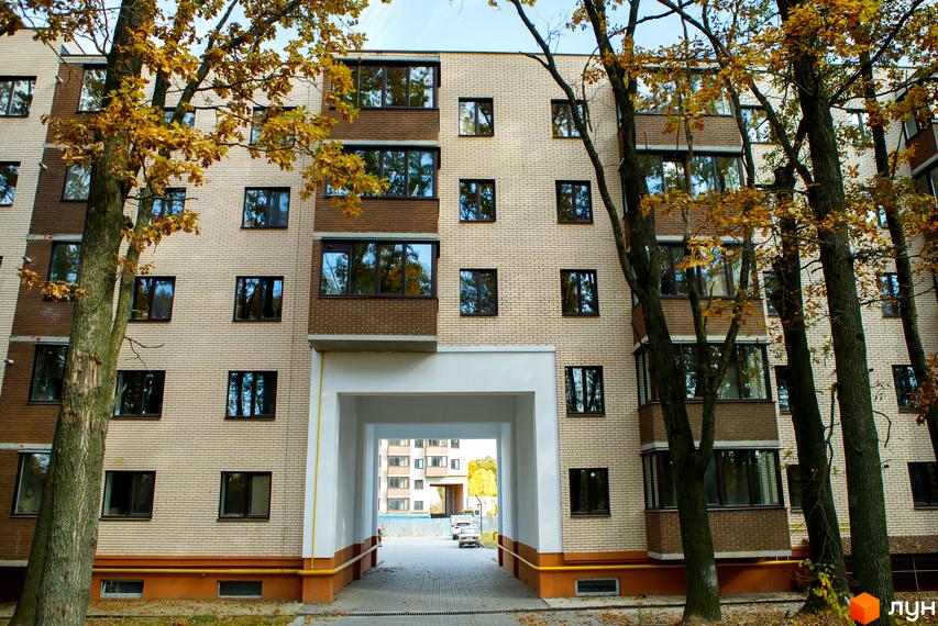 Фасад житлового комплексу Софія з цегляним оздобленням та великими вікнами. Навколо будинку ростуть дерева з осіннім листям, а через арку видно іншу будівлю.