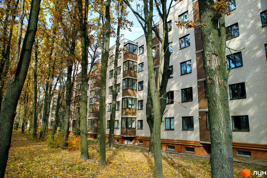 Зовнішній вигляд будинку ЖК Софія з цегляним фасадом та балконами, оточений деревами з осіннім листям. Прибудинкова територія вкрита опалим листям.