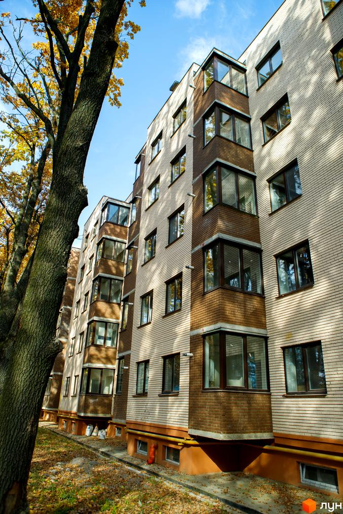 Фасад житлового комплексу Софія з цегляним оздобленням та скляними балконами. Навколо будинку дерева з жовтим листям та осіннє листя на землі.