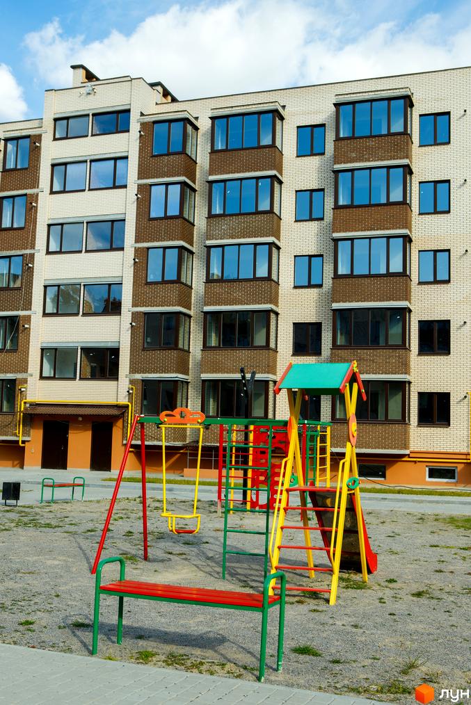 Зовнішній вигляд будинку ЖК Софія з цегляним оздобленням та великими вікнами. На прибудинковій території розташований дитячий майданчик з гойдалками та гіркою.