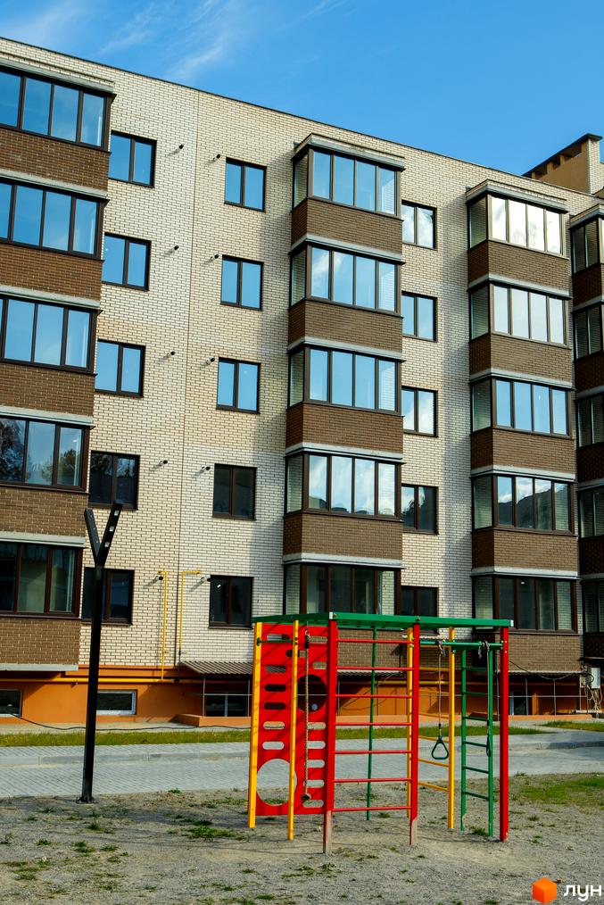 Зовнішній вигляд новобудови ЖК Софія з цегляним фасадом та балконами. На прибудинковій території розташований дитячий майданчик з яскравими елементами.