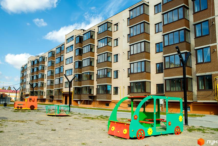 Новобудова ЖК Софія з цегляним фасадом та балконами. Поруч дитячий майданчик з ігровими елементами.