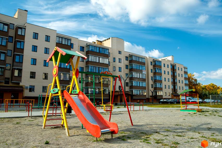 Житловий комплекс Софія. Зовнішній вигляд будинку з цегляним фасадом та балконними блоками. Прибудинкова територія з дитячим майданчиком та пісочницею.