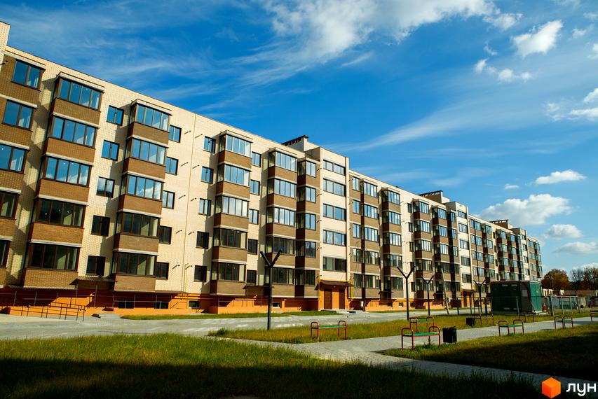 Зовнішній вигляд новобудови ЖК Софія з цегляним фасадом та великими вікнами. Прибудинкова територія з зеленими газонами та доріжками.