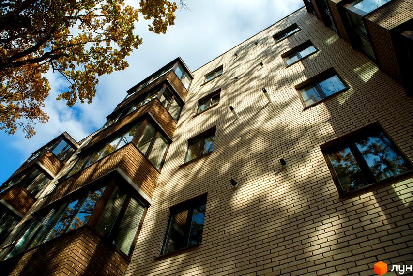 Фасад житлового комплексу Софія з цегляним оздобленням та скляними балконами. Вид знизу на будівлю з деревами та небом.