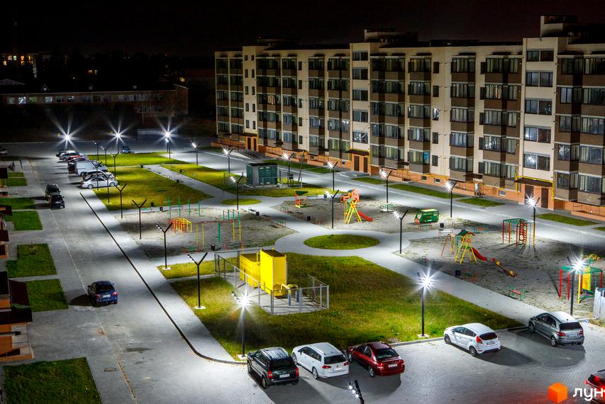 Житловий комплекс Софія вночі. Сучасні багатоповерхові будинки з освітленими вікнами та доглянутою прибудинковою територією з дитячими майданчиками та парковкою.