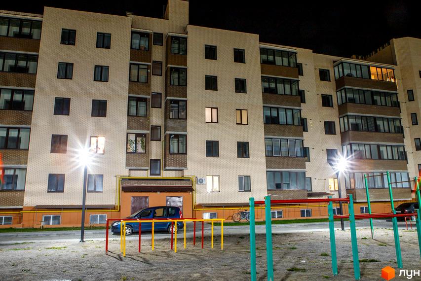 Зовнішній вигляд багатоповерхового житлового комплексу Софія вночі. На прибудинковій території видно дитячий майданчик та припаркований автомобіль.