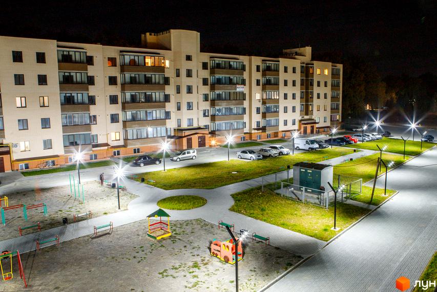 Зовнішній вигляд нового житлового комплексу Софія вночі. На території розташований дитячий майданчик та парковка з автомобілями.