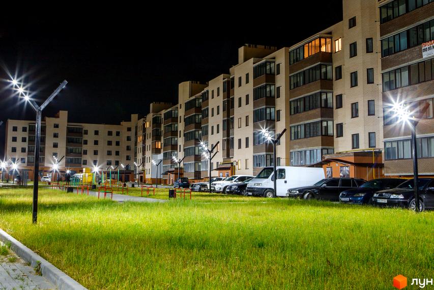 Житловий комплекс Софія. Зовнішній вигляд цегляних будинків з коричневими елементами та балконами. Прибудинкова територія з газоном, парковкою та освітленням.