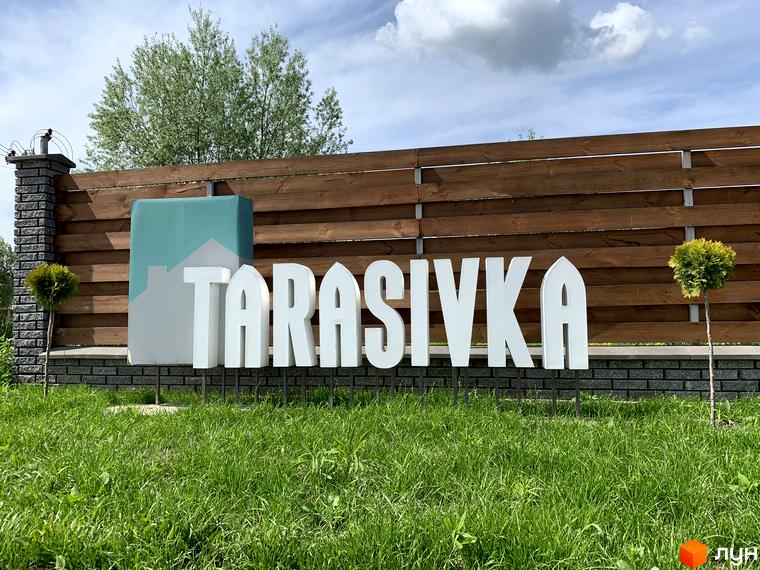 Котеджне містечко Тарасівка: білі об'ємні літери на фоні дерев'яного паркану та зеленої галявини. Зовнішній вигляд новобудови та прибудинкової території.