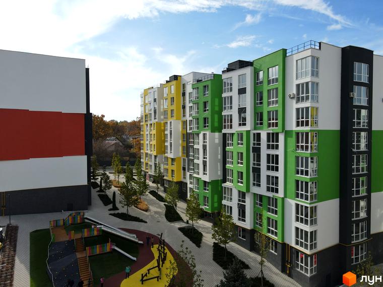 Житловий комплекс Синергія-3+: фасади будівель у білому, зеленому та жовтому кольорах, дитячий майданчик та доглянута прибудинкова територія.