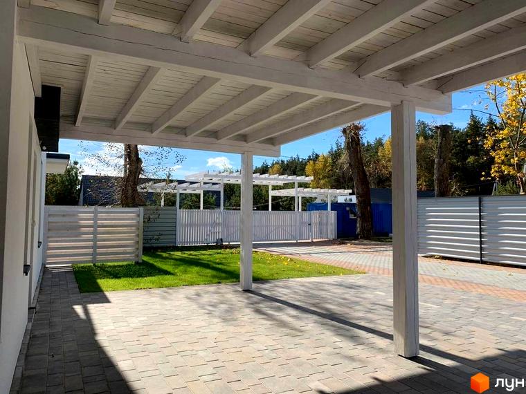 Котеджне містечко КМ Wood Side Village. Білий навіс над терасою, бруківка та зелений газон.