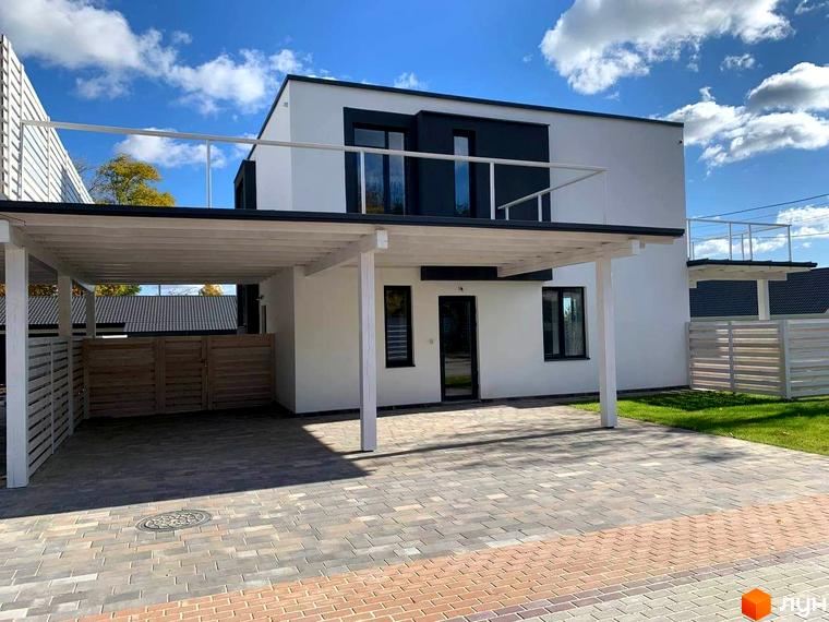 Котеджне містечко КМ Wood Side Village: двоповерховий будинок з білою фасадною частиною, темними вікнами та балконами, поруч розташована крита парковка та огороджена територія.