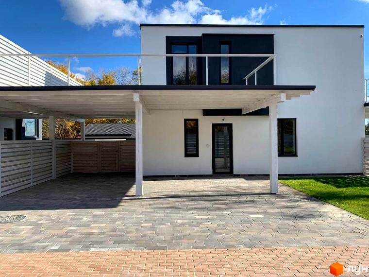 Котеджне містечко K.M. Wood Side Village. Фото фасаду двоповерхового будинку з навісом для авто та вимощеною територією.